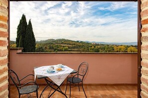 Ein Balkon mit Tisch für zwei Personen, mit Blick auf eine reizvolle Landschaft mit Hügeln und Bäumen.