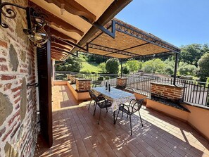 An outdoor patio with a table and chairs, a pergola, and a view of the surrounding landscape.