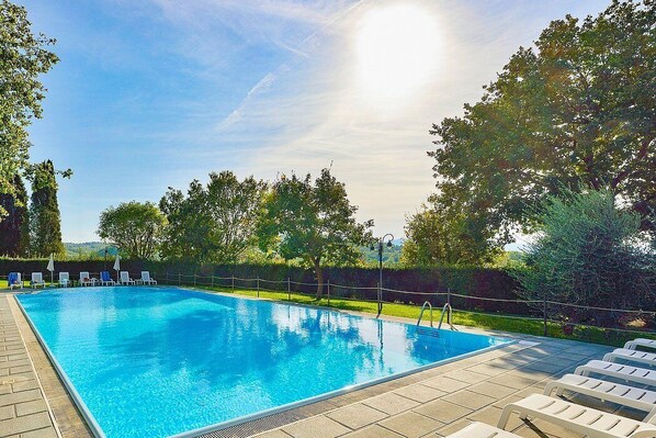 Ein rechteckiger Swimmingpool mit klarem, blauem Wasser, umgeben von einer gefliesten Liegefläche und weißen Liegestühlen.
