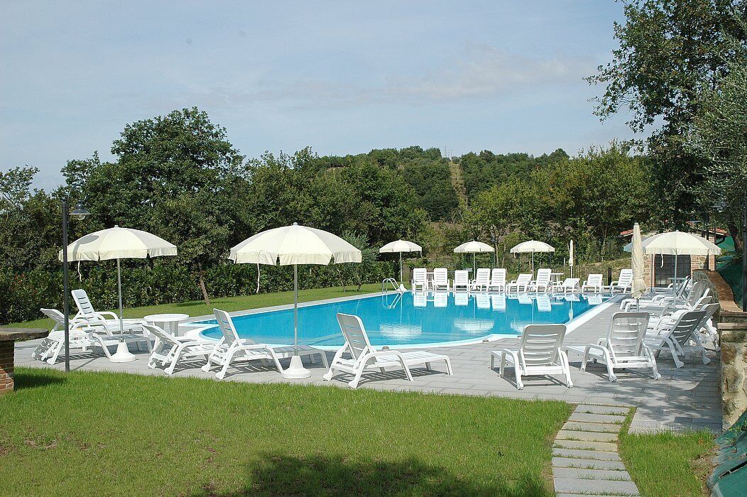 Une piscine entourée de verdure, avec des chaises longues blanches et des parasols.