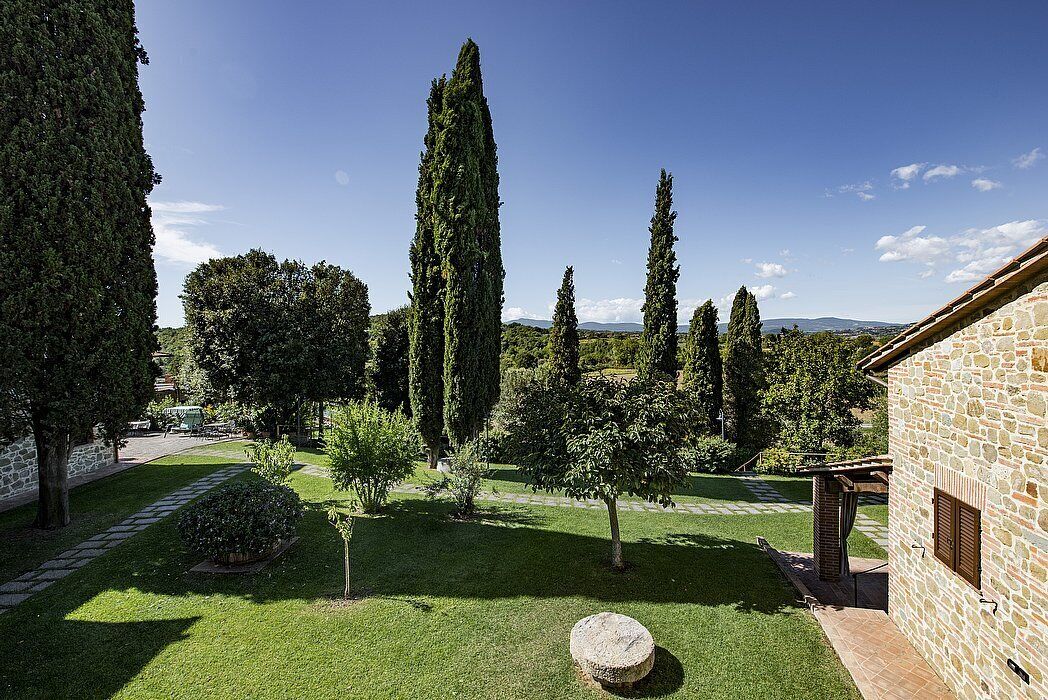 A courtyard with stone walls, a stone building, and a variety of trees.