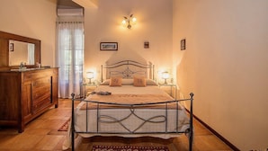 Quarto com cômoda de madeira, cama com estrutura de metal e luminária fixada na parede.