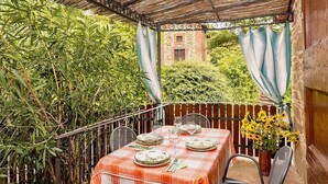 A covered outdoor dining area with a table set for four, surrounded by greenery and a brick building in the background. - Casa Caprifoglio F: A characteristic and welcoming apartment that is part of an ancient country house surrounded by the greenery, with Free WI-FI. (Città della Pieve)