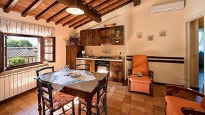 A kitchen with wooden cabinets, a dining table set for four, and a view of a garden through a window. - Casa Caprifoglio F: A characteristic and welcoming apartment that is part of an ancient country house surrounded by the greenery, with Free WI-FI. (Città della Pieve)
