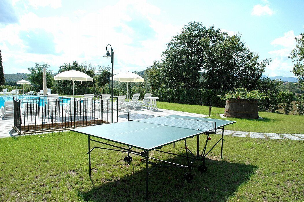 An outdoor area with a ping pong table, lounge chairs, and a pool.