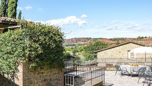A stone building with a metal balcony, outdoor seating, and a view of hills.
