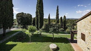 Une cour bordée de murs en pierre, un bâtiment en pierre et une variété d’arbres.