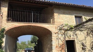 A stone archway leading to a building with a tiled roof and a barred balcony.