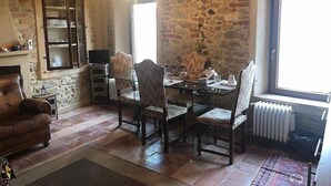 A rustic room with a stone wall, a fireplace, a dining table with chairs, and a sofa.