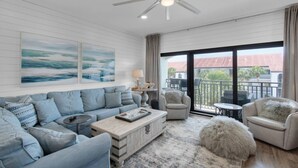 A spacious living room with a high ceiling fan, a large window with a view of the outside, and a cozy seating area with a coffee table and ottoman. - Private Beach | 1 minute walk to Beach! | Beautifully updated 1 bedroom condo | Sleeps 6 | Wi-Fi (Santa Rosa Beach)
