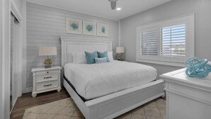 A bedroom with a white bed, two bedside tables with lamps, a ceiling fan, a window with blinds, and a decorative glass sculpture on a dresser. - Private Beach | 1 minute walk to Beach! | Beautifully updated 1 bedroom condo | Sleeps 6 | Wi-Fi (Santa Rosa Beach)