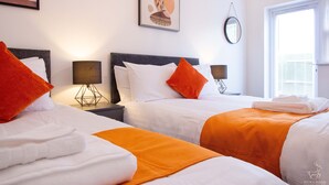 Een hotelkamer met twee bedden, elk voorzien van wit en oranje beddengoed, een nachtkastje met lamp en kunst aan de wanden.