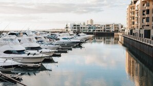 A marina with multiple yachts docked along a calm waterway, surrounded by modern buildings with balconies. - Glenelg Beach House With Private Beachfront Pool (Glenelg North)