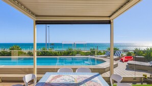Ein Poolbereich mit Meerblick, eine überdachte Sitzgelegenheit und ein Tisch mit Mosaik-Tischdecke.