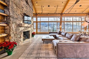 A spacious living room with a stone wall, a fireplace, leather sofas, and large windows offering a view of the outdoors. - 13 Mi to Slopes! Silverthorne Home w/ Pool Access (Silverthorne)