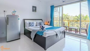 Un dormitorio moderno con cama, refrigerador, ventana con cortinas y balcón con mobiliario exterior.