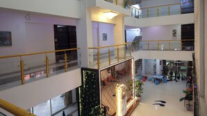Un atrio de varios niveles con barandillas de cristal, un área decorativa central con plantas y una escalera que conecta los pisos.