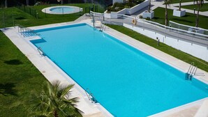 A rectangular swimming pool with a white deck, surrounded by a white fence and palm trees.