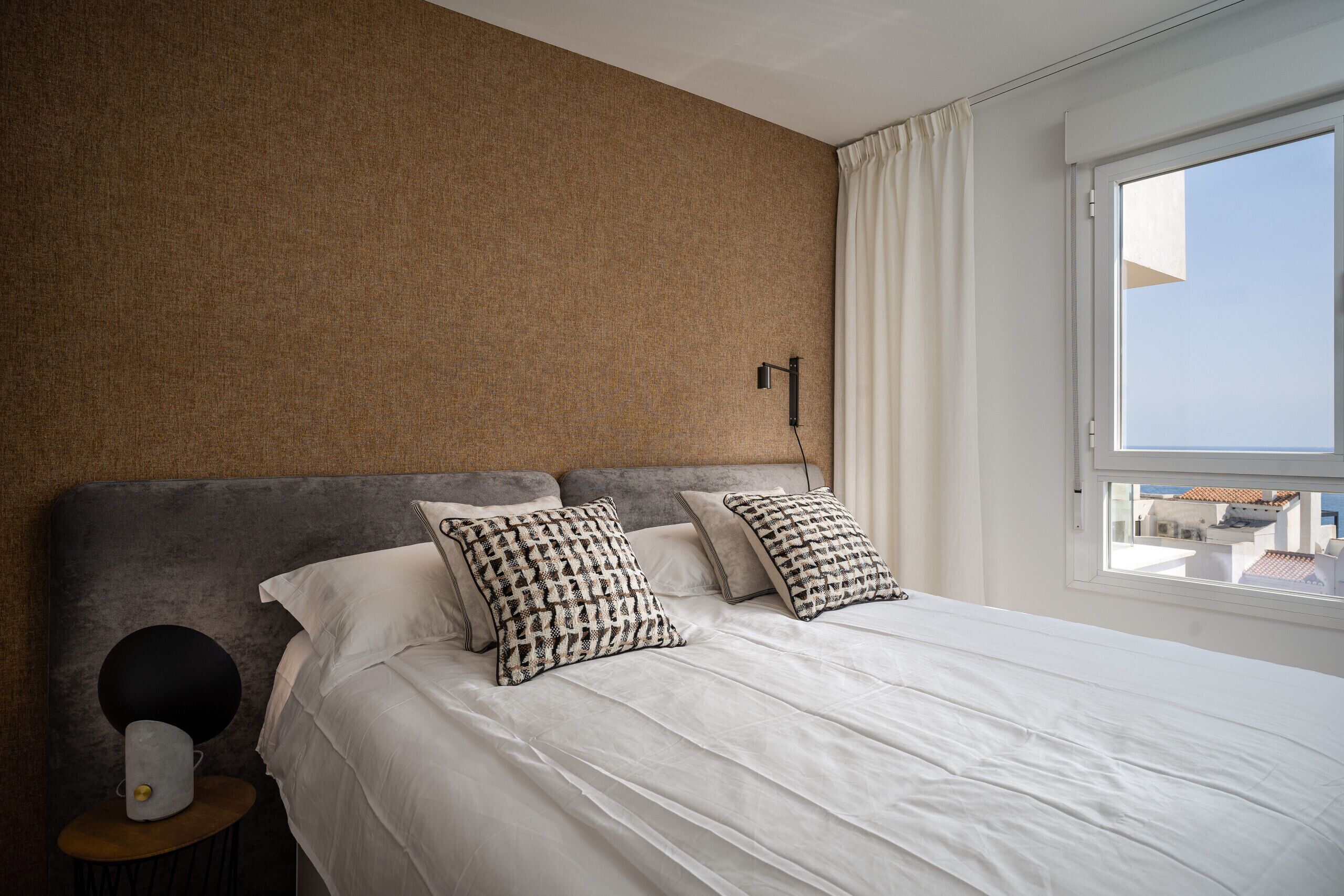 A bedroom with a large bed, two pillows, a bedside lamp, and a view of the sky through a window.