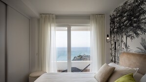 A hotel room with a bed, a view of the ocean, and a tropical mural.