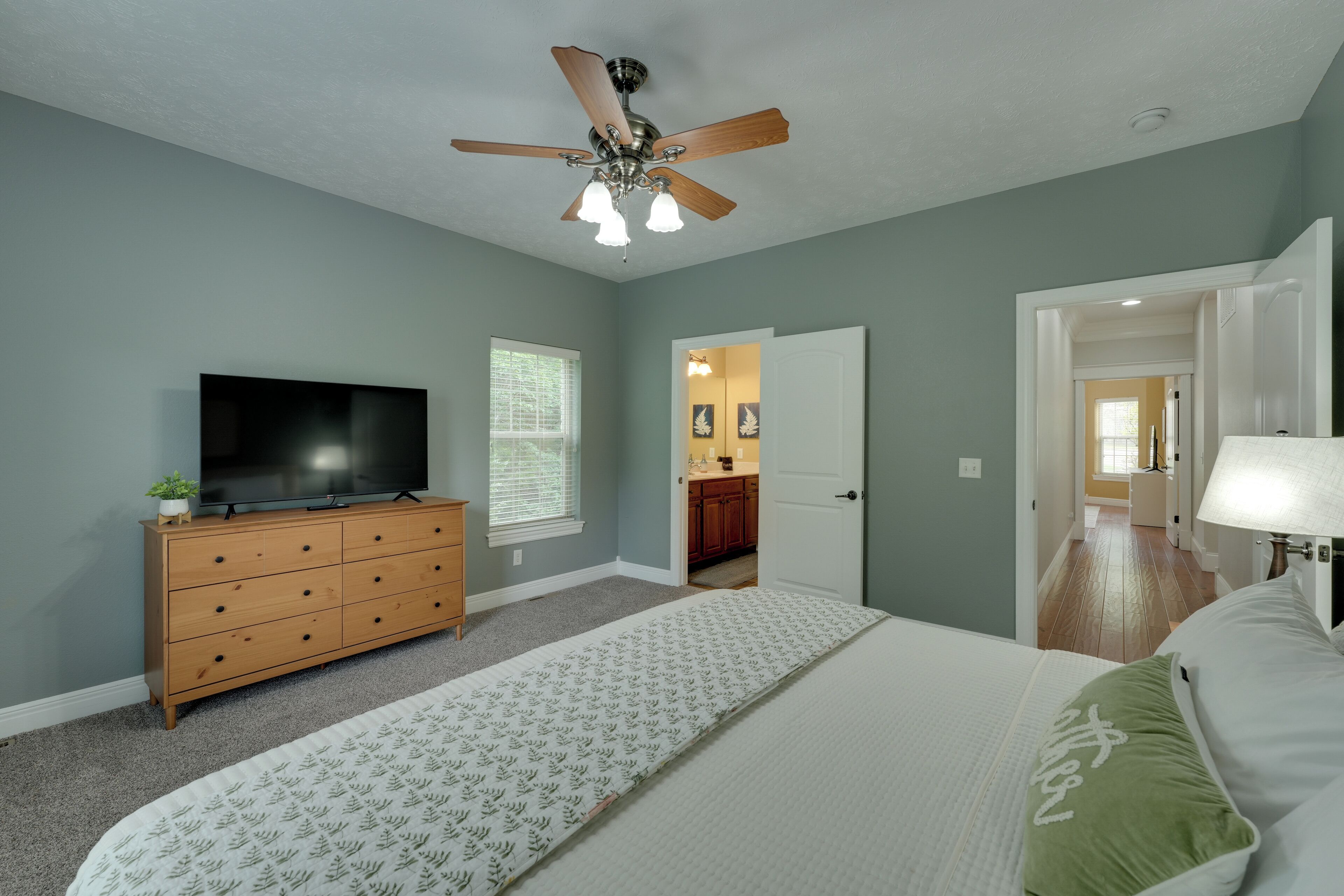 Ein Schlafzimmer mit Bett, Fernseher, Kommode, Deckenventilator und einer Tür zu einem Badezimmer.