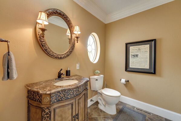 Une salle de bain avec un lavabo en marbre, deux appliques murales, un document historique encadré et des toilettes.