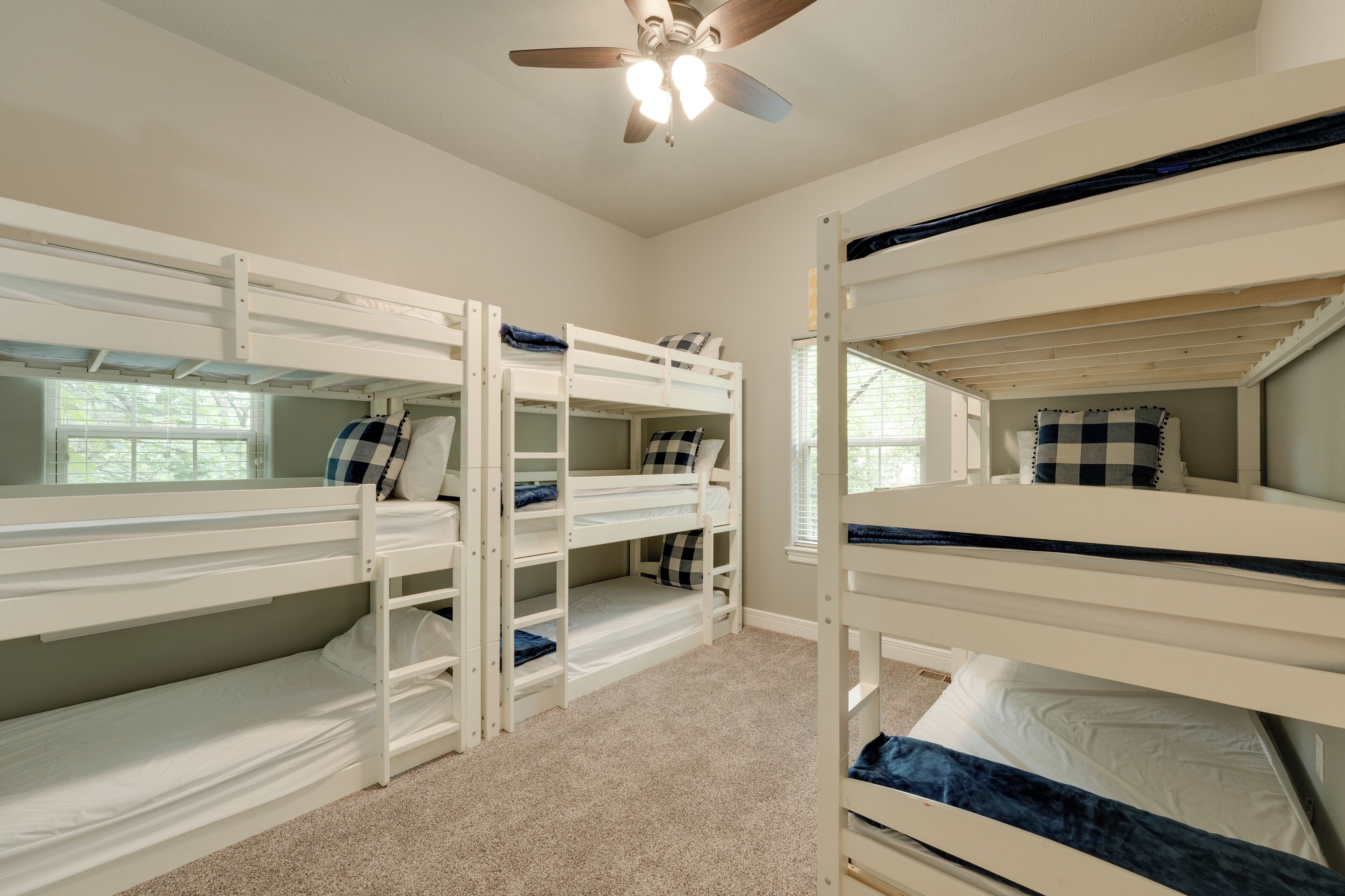 A room with bunk beds, a ceiling fan, and a window with blinds.