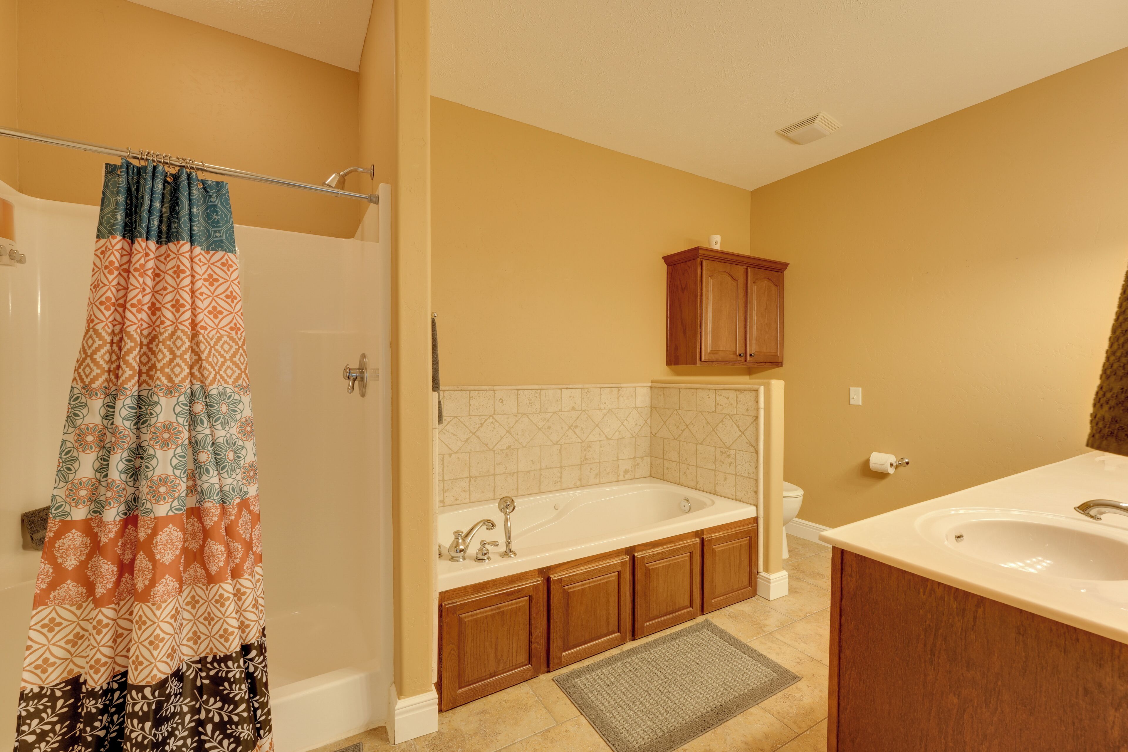 A bathroom with a bathtub, a sink, wooden cabinets, and a patterned shower curtain.