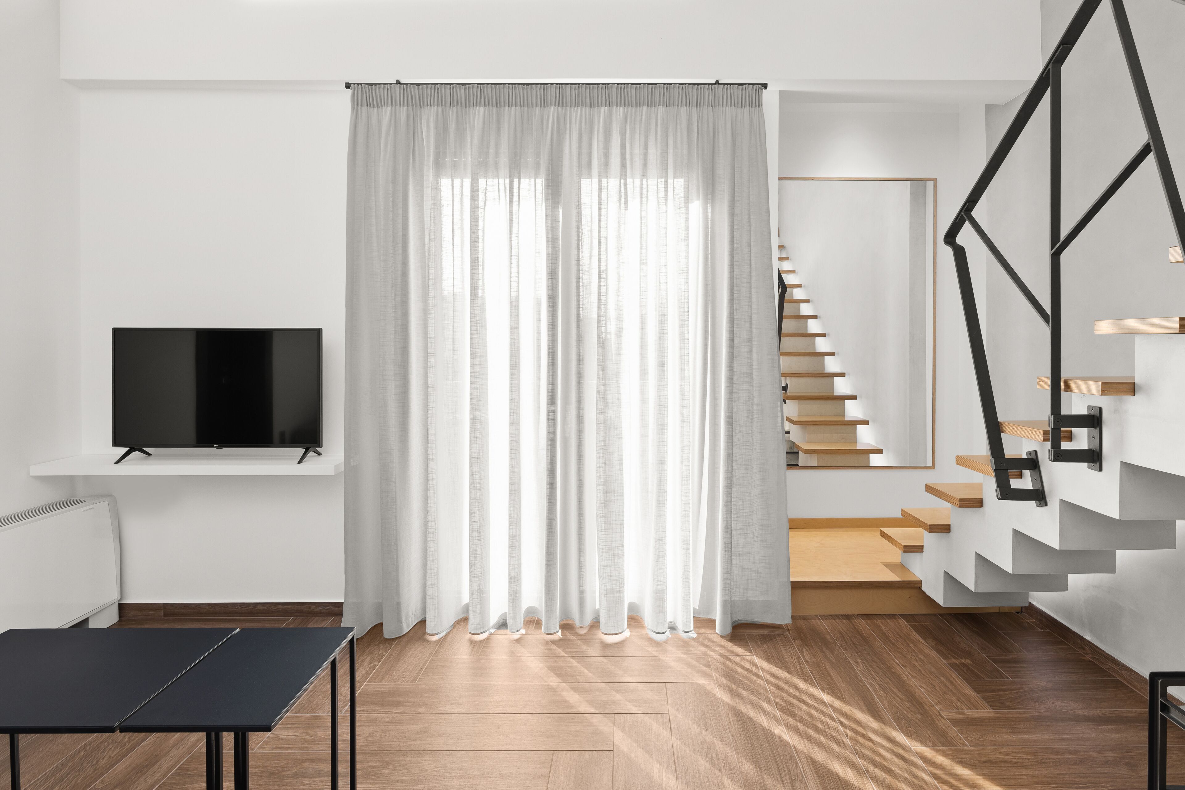 A modern living room with a flat-screen TV, a black table, and a staircase with wooden steps and a metal railing.