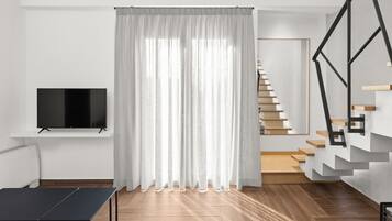 Een moderne woonkamer met een flatscreen televisie, een zwarte tafel en een trap met houten treden en een metalen leuning.
