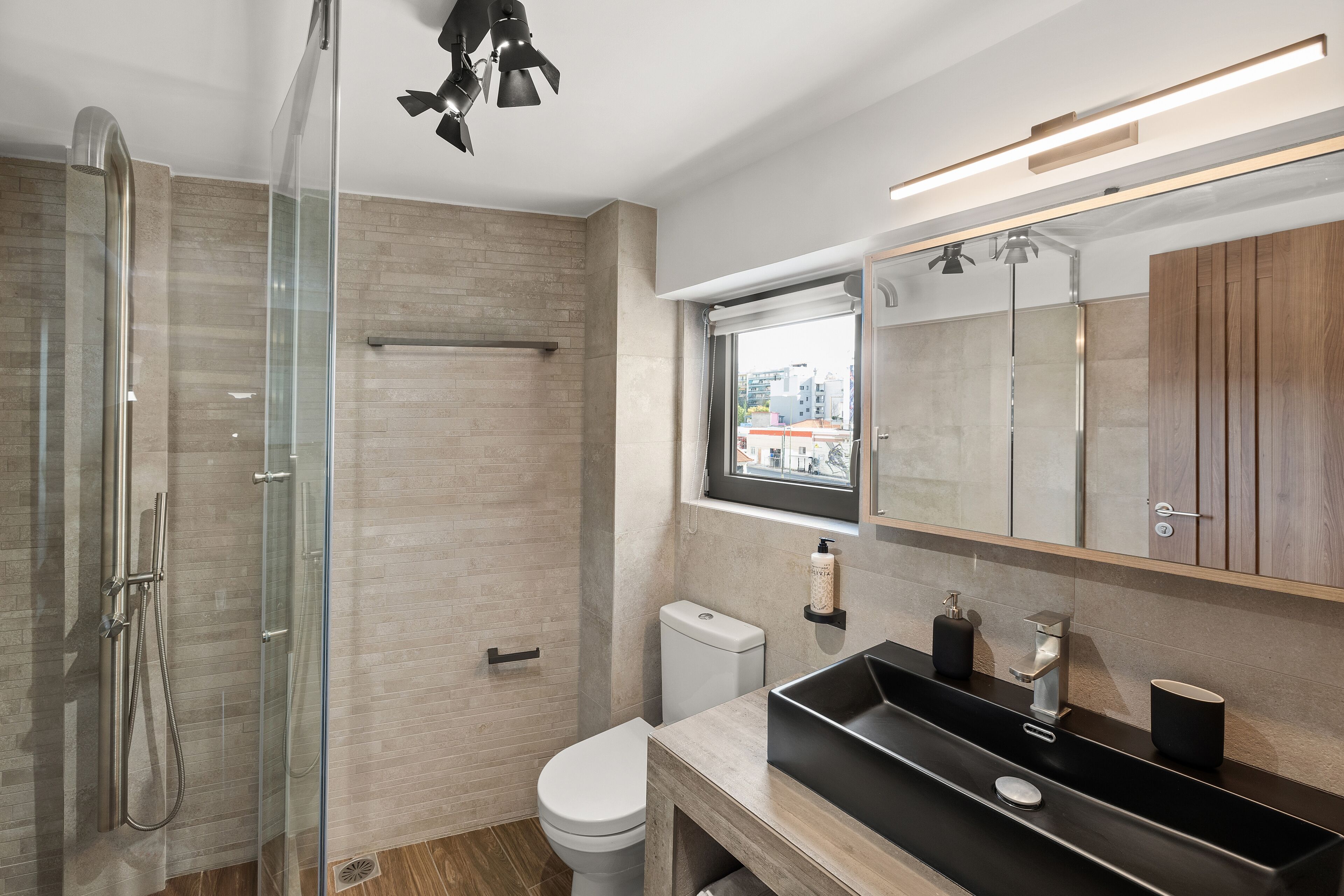 A modern bathroom with a glass-enclosed shower, a white toilet, and a black sink with a wooden vanity.