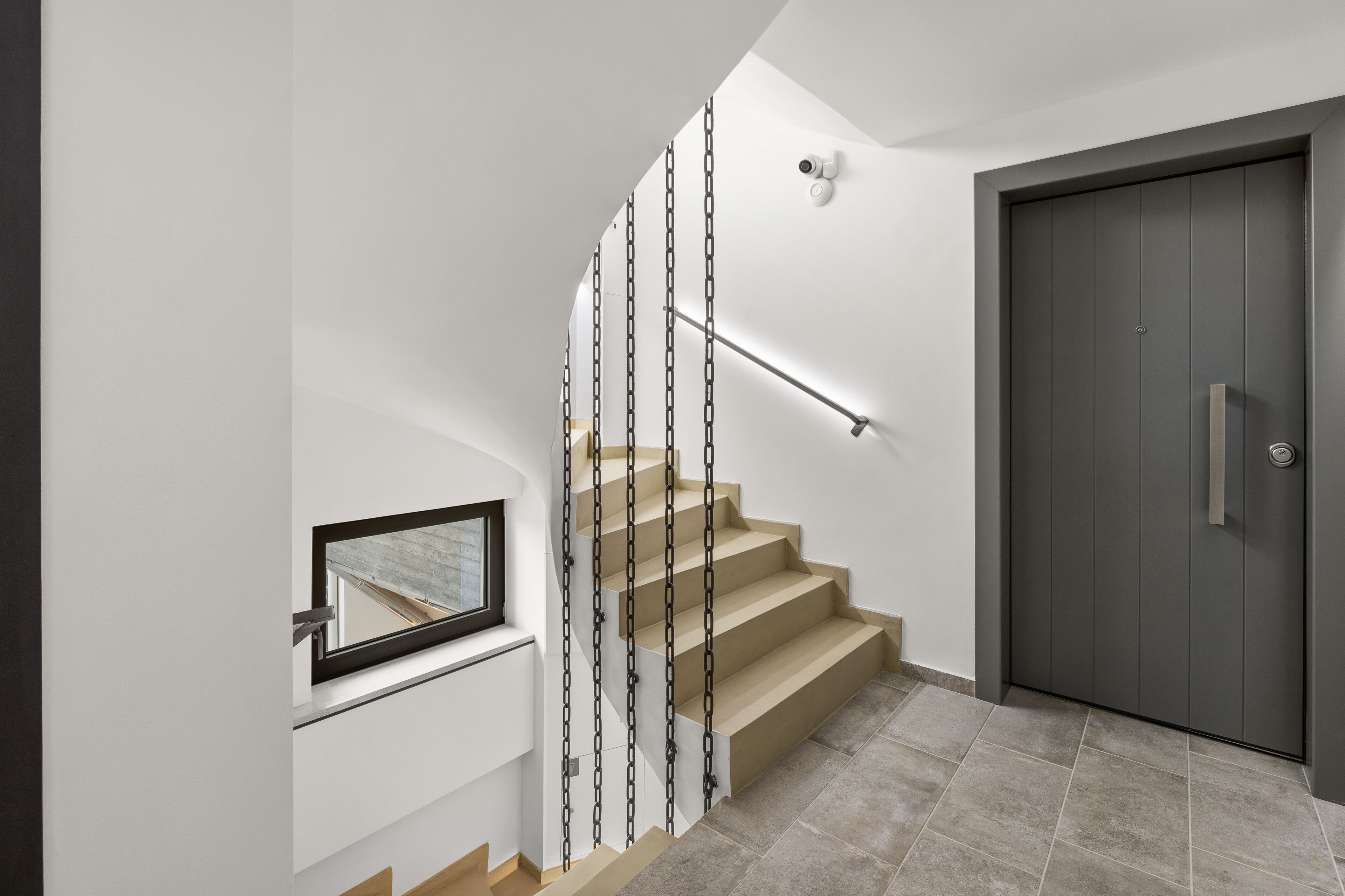 Una escalera moderna con barandilla de cristal, una puerta y una ventana.