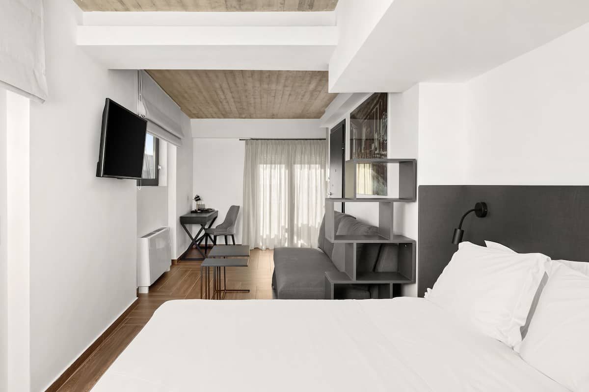 A modern hotel room with a bed, a desk, a chair, a TV, and a window with curtains.