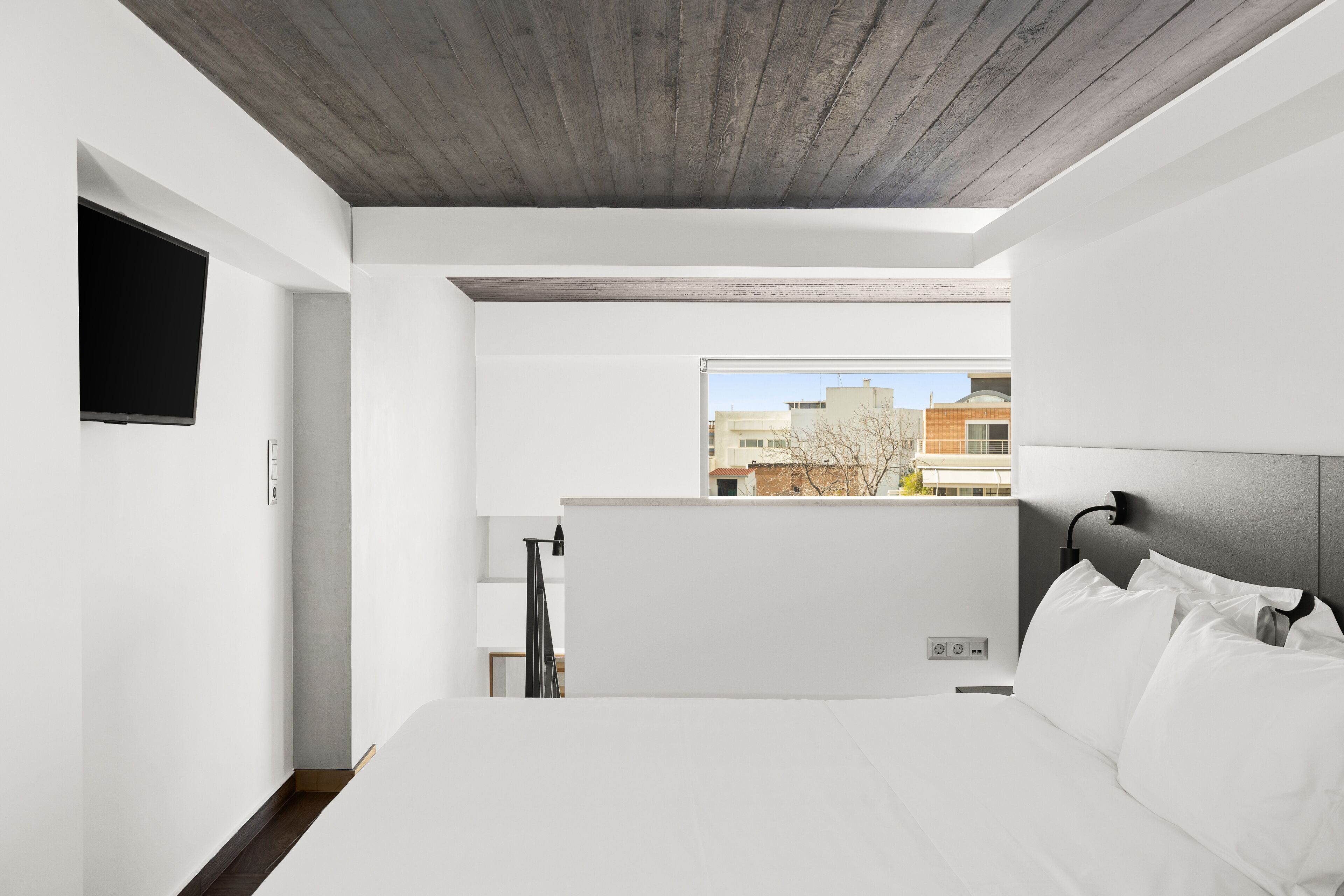 Quarto de hotel moderno com uma cama grande, televisão de tela plana na parede e vista para a cidade pela janela.