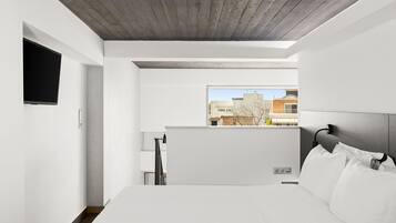 Quarto de hotel moderno com uma cama grande, televisão de tela plana na parede e vista para a cidade pela janela.