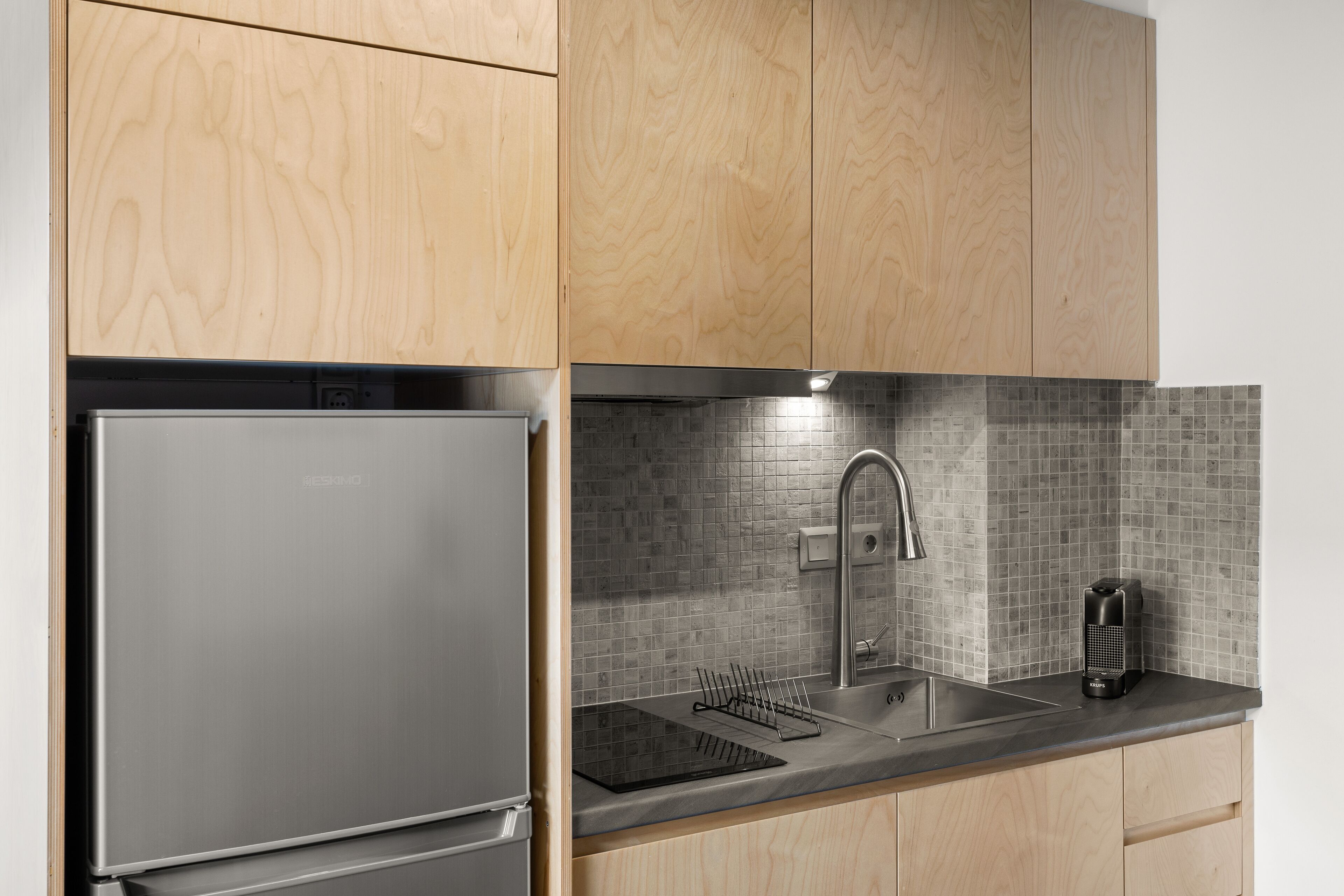 A kitchen with wooden cabinets, a stainless steel refrigerator, a tiled backsplash, a sink, and a coffee maker.