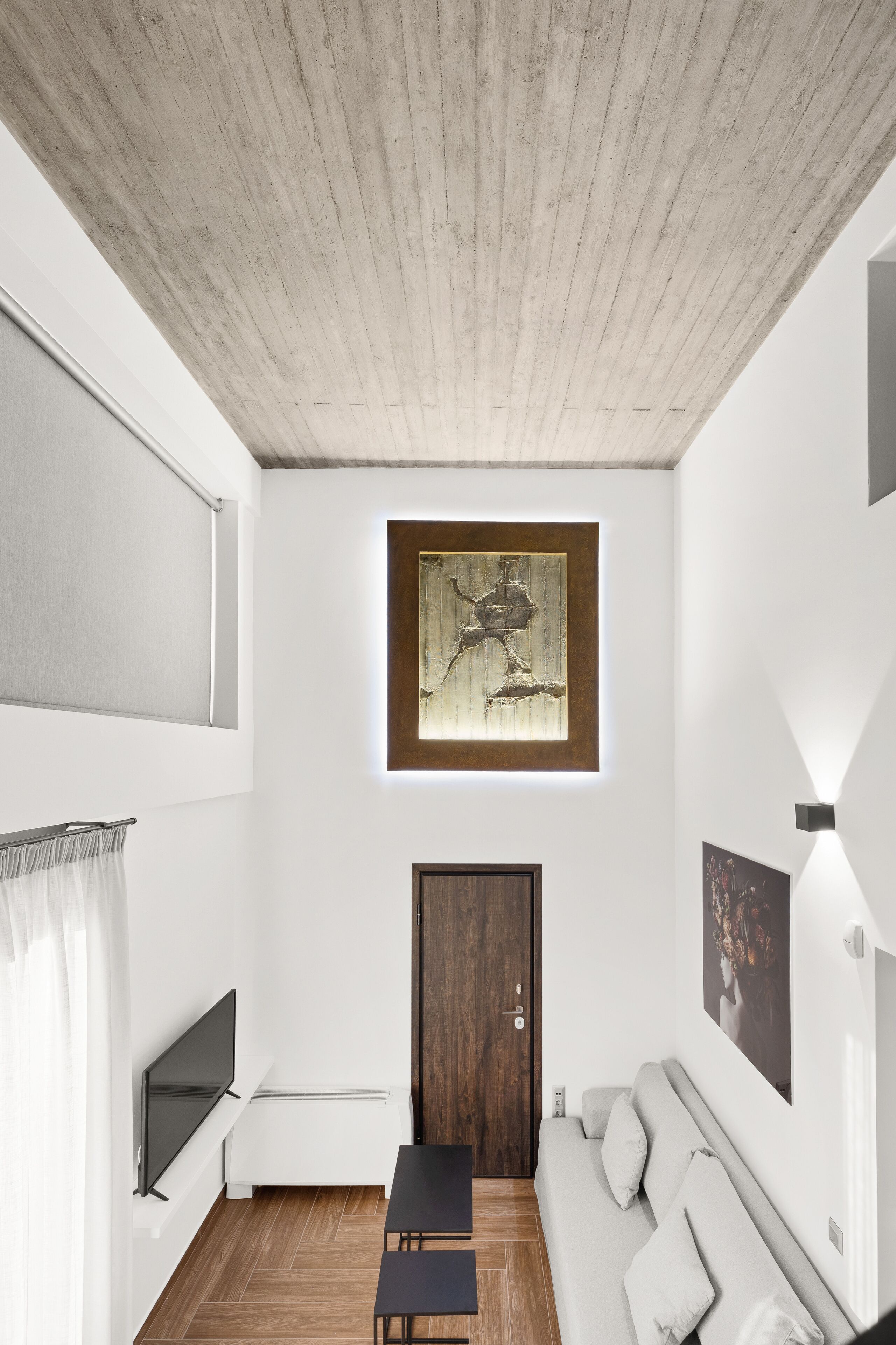 Uma sala de estar moderna com teto de madeira, uma obra de arte pendurada, sofá, televisão e porta.