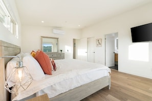 A bedroom with a bed, a bedside lamp, a television, and a door leading to another room.