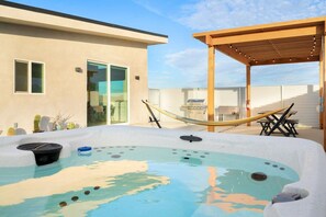 A hot tub with a wooden pergola and a hammock in a backyard setting. - Sun Oro - Hot Tub, BBQ, Fire Pit and Gameroom (Joshua Tree)