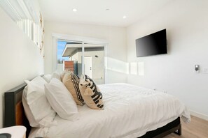 A bedroom with a bed, a television mounted on the wall, and a door leading to an outdoor area. - Sun Oro - Hot Tub, BBQ, Fire Pit and Gameroom (Joshua Tree)