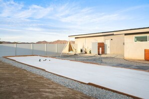 A modern building with a flat roof, a covered outdoor area with a white surface, and a gravel path leading to the entrance.
