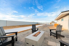 An outdoor patio area with a fire feature, seating, and a view of the sky.