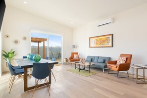 A modern living room with a dining area, a sofa set, and a large window with a view.
