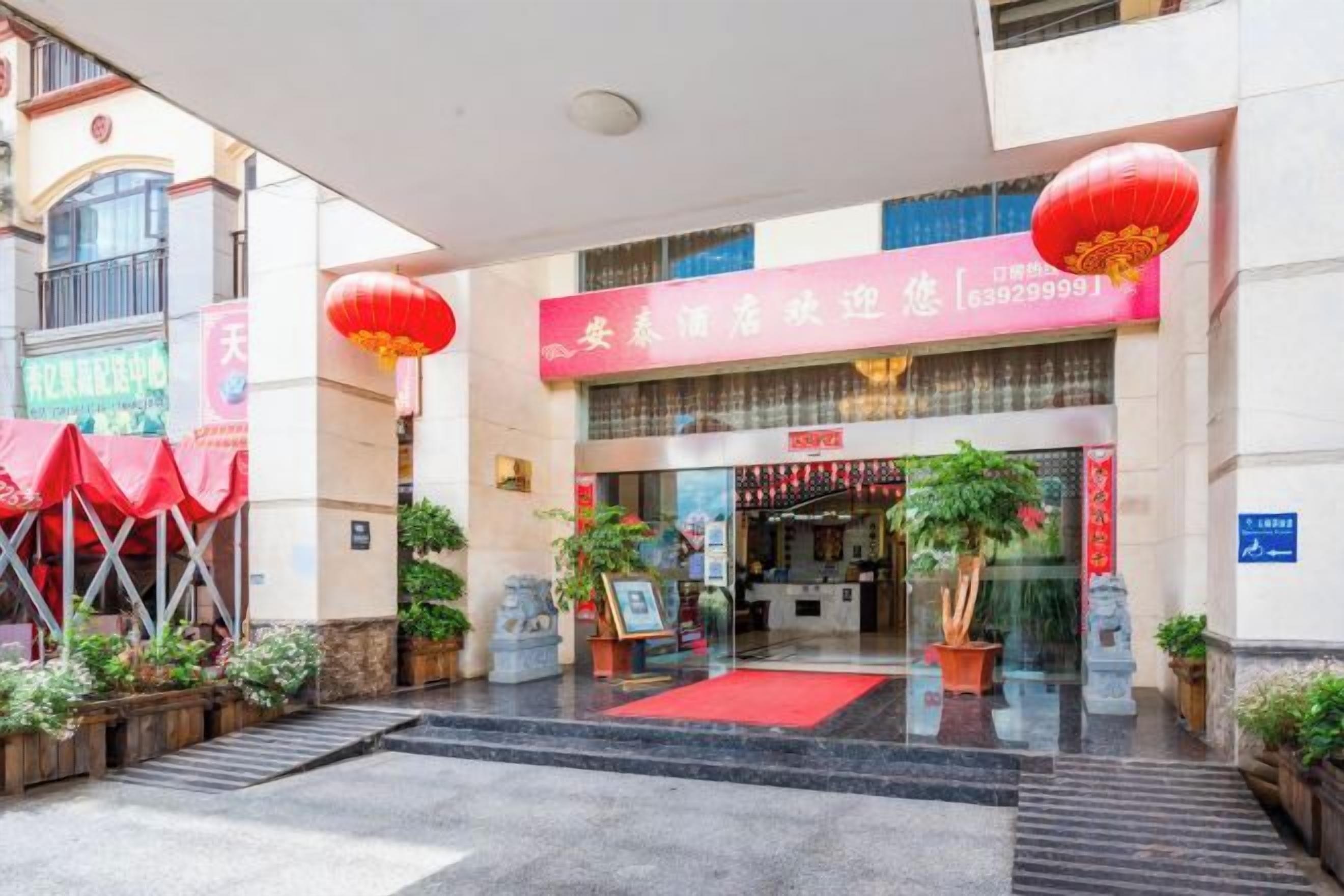 L’entrée d’un hôtel, avec un auvent rouge, une lanterne rouge et un tapis rouge menant à la porte.