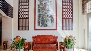 Une pièce au décor traditionnel, avec un canapé en bois, deux plantes en pot et une grande œuvre d’art encadrée accrochée au mur.