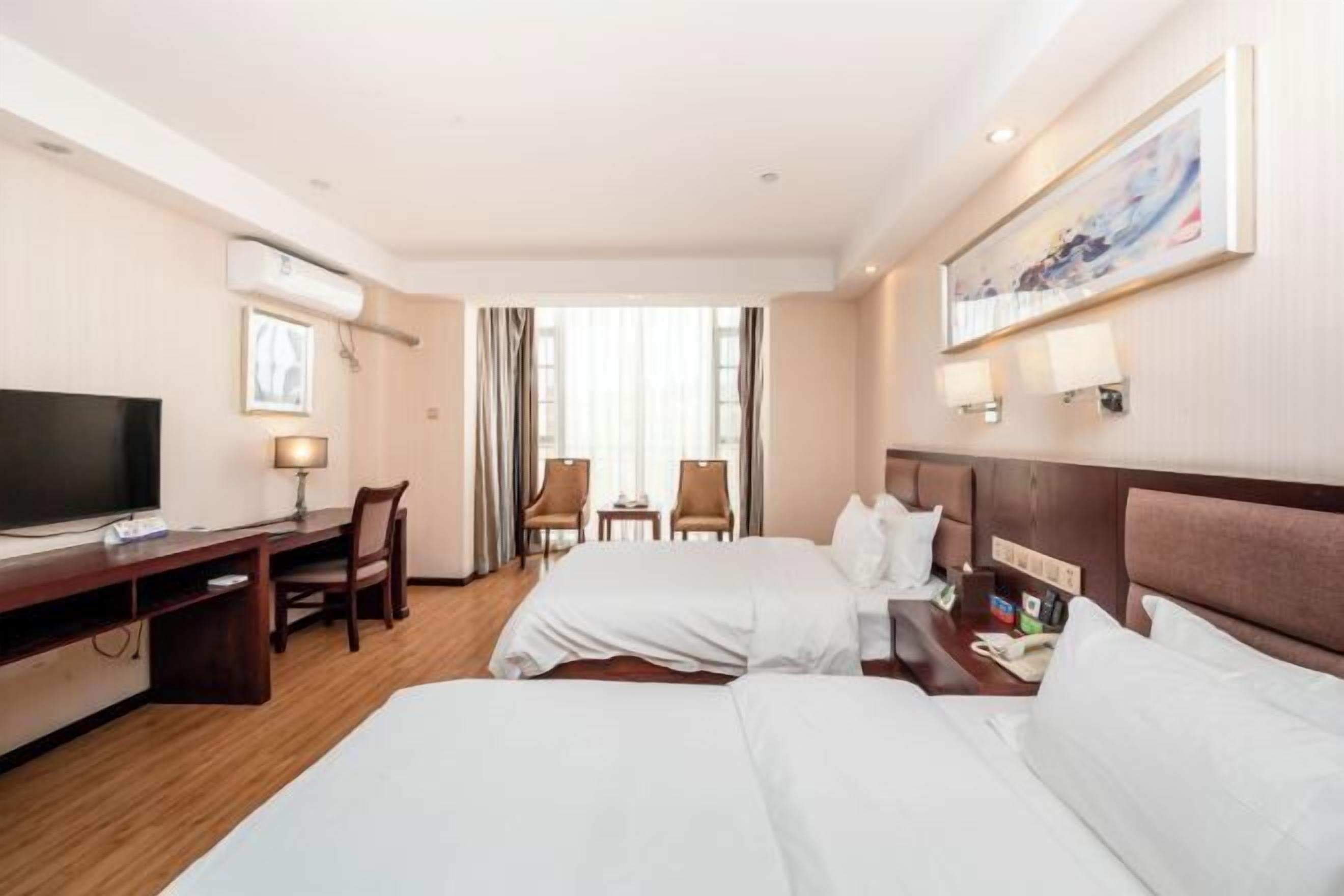 A hotel room with two beds, a desk, a TV, and a painting on the wall.