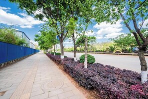 A paved walkway with trees and shrubs, bordered by a blue fence and a road. - Antai Hotel (Anning)