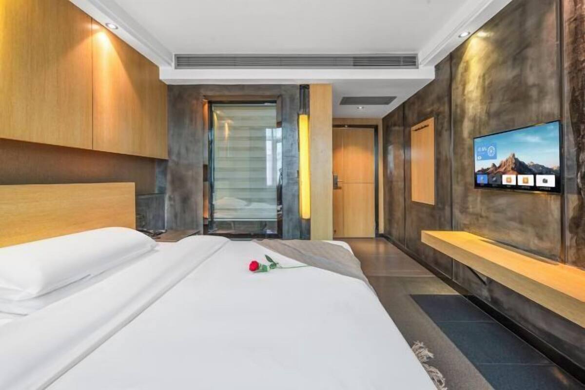 A modern hotel room with a large bed, a TV mounted on the wall, and a staircase leading to another room.