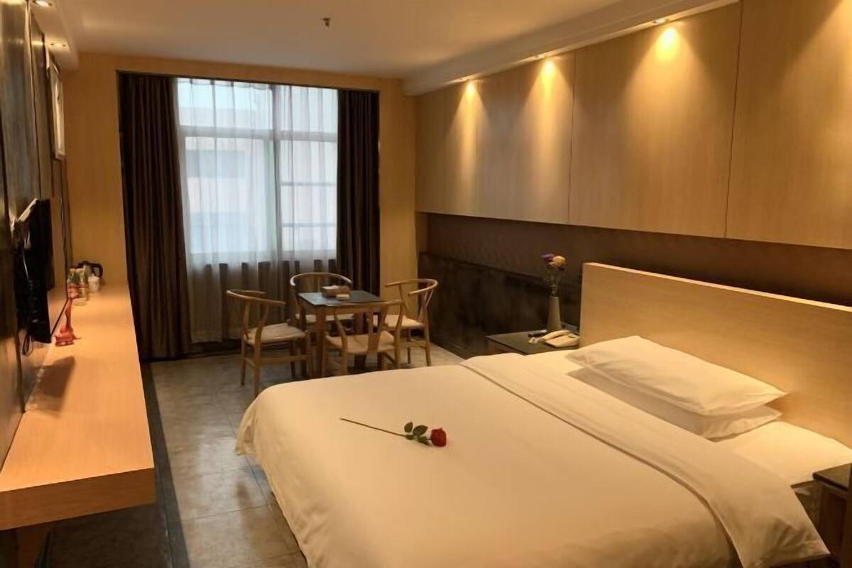 A hotel room with a bed, a desk, a chair, a TV, and a window with curtains.