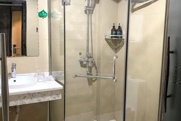 Un baño moderno con cabina de ducha de vidrio, un lavabo blanco y un estante pequeño con artículos de aseo.